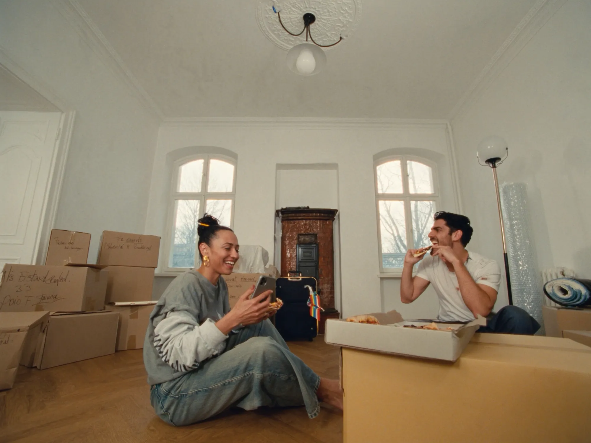 A couple sharing a pizza among moving boxes in their new flat
